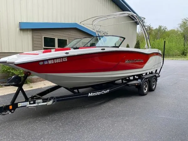 The Image of 2017 MasterCraft NXT22 boat in red and white on a trailer, parked outdoors. - 0