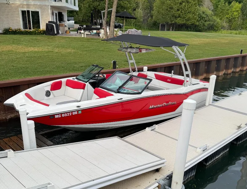 Slide: The Image of 2017 MasterCraft NXT22 boat docked, red and white design, near a lakeside house. - 2