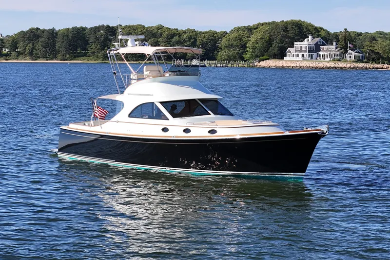 Slide: The Image of 2005 San Juan SJ 48 Flybridge yacht cruising on a scenic lake with a shoreline view. - 5