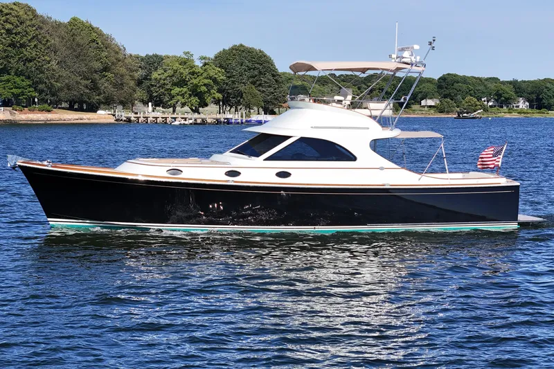 Slide: The Image of 2005 San Juan SJ 48 Flybridge yacht on serene water with lush green shoreline. - 6