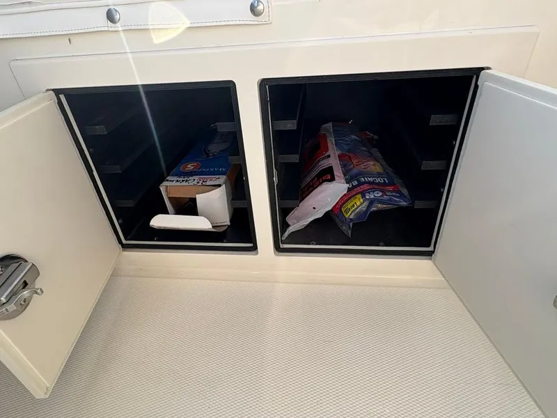Slide: The Image of Open storage compartments on a 2014 Carolina Classic 25 boat, containing various items. - 16
