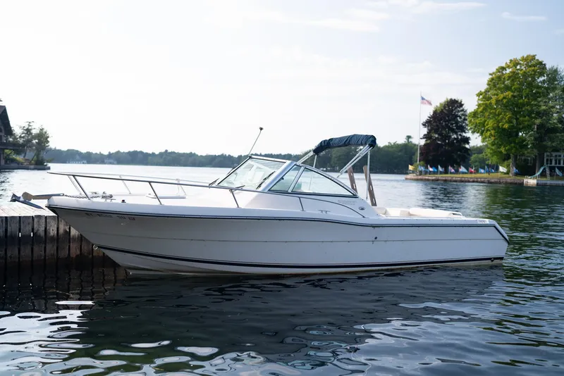 Slide: The Image of 2001 Pursuit 2460 Denali boat docked on a calm lake with trees in the background. - 0