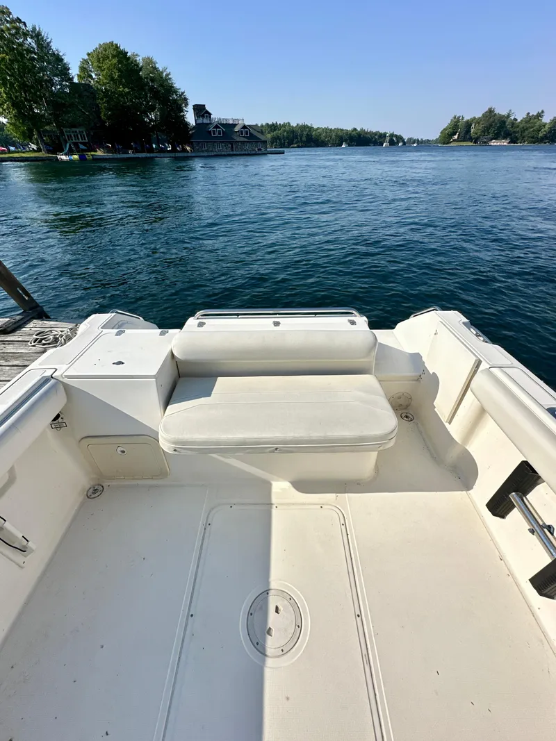 Slide: The Image of 2001 Pursuit 2460 Denali boat interior with seating, docked by a scenic lake. - 4