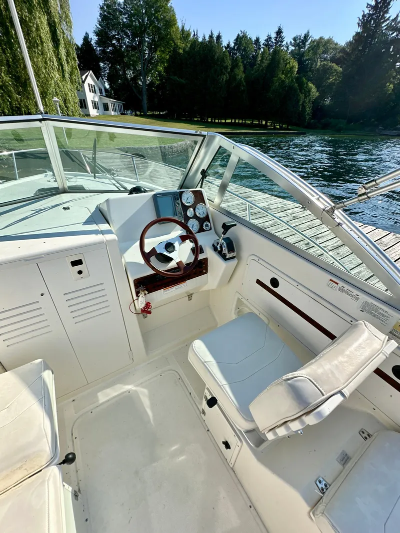 Slide: The Image of 2001 Pursuit 2460 Denali boat interior with steering wheel, dashboard, and seating by a lake. - 8