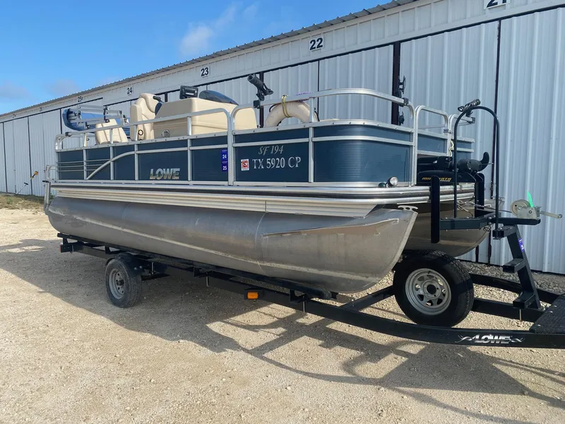 Slide: The Image of 2014 Lowe SF194 Sport Fish pontoon boat on trailer, parked outside storage units. - 1