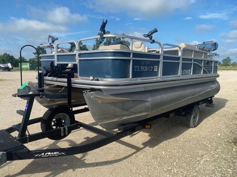 Slide: The Image of 2014 Lowe SF194 Sport Fish pontoon boat on trailer, parked outdoors under blue sky. - 2