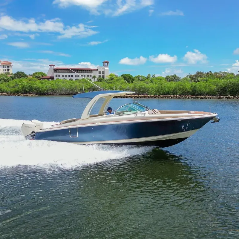 Slide: The Image of 2023 Chris-Craft Launch 31 GT cruising on a scenic waterway under a clear blue sky. - 0