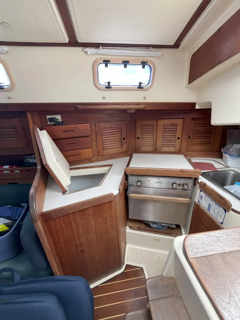 Slide: The Image of 1988 Tartan 31 yacht interior with wooden cabinetry and compact kitchen area. - 11