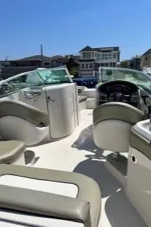 Slide: The Image of 2006 Sea Ray 220 Sundeck boat interior with seating and steering wheel, docked near waterfront homes. - 4