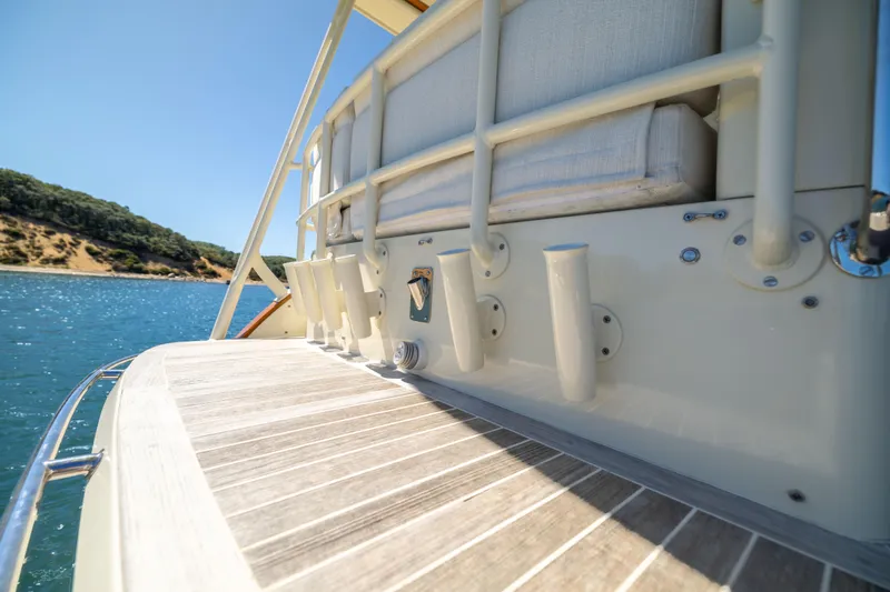Slide: The Image of 2014 Hinckley Talaria 48 Flybridge yacht deck with rod holders, near scenic shoreline. - 10