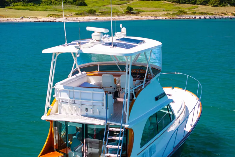 Slide: The Image of 2014 Hinckley Talaria 48 Flybridge yacht on clear blue water, near a scenic shoreline. - 5