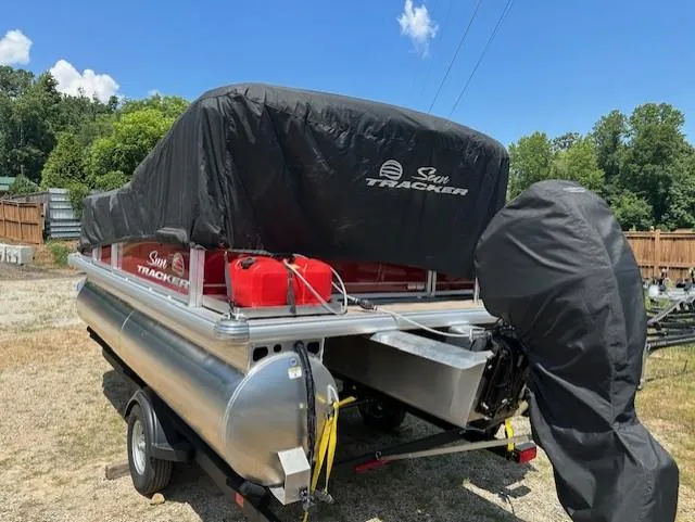 Slide: The Image of 2024 Sun Tracker Bass Buggy 16 XL Select pontoon boat covered, parked outdoors. - 17