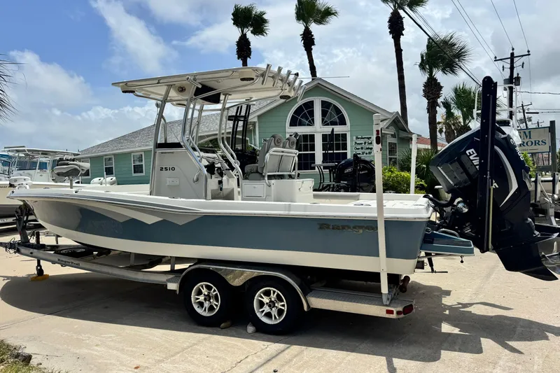 Slide: The Image of 2016 Ranger 2510 Bay Ranger boat on trailer, parked near palm trees and a house. - 2