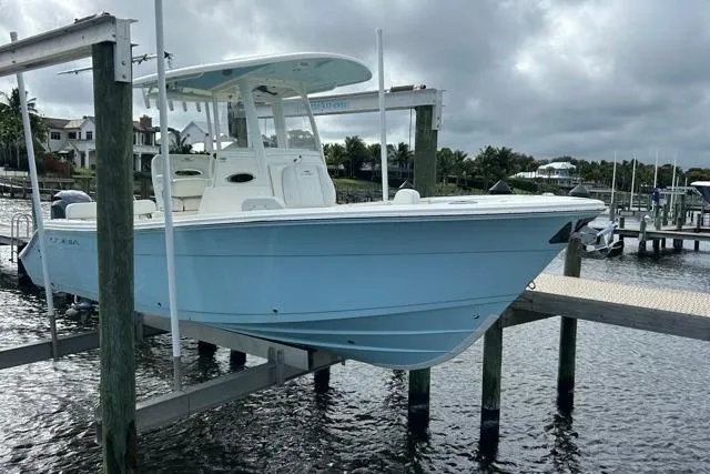 Slide: The Image of 2022 Cobia 240 Center Console boat on lift, docked at marina under cloudy sky. - 30