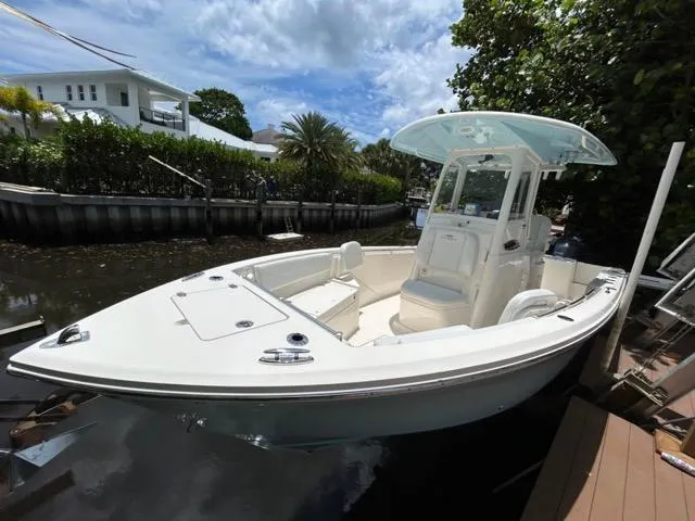 Slide: The Image of 2022 Cobia 240 Center Console boat docked near waterfront home, surrounded by lush greenery. - 6