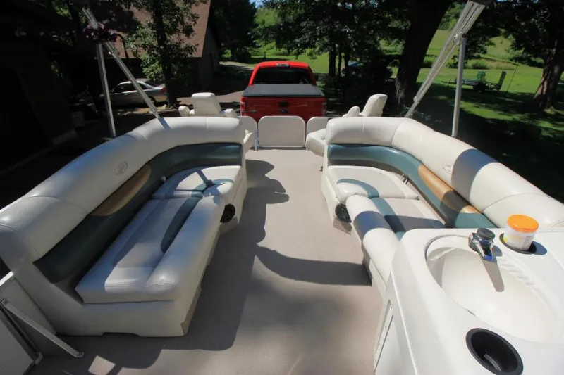 Slide: The Image of 2002 Princecraft Versailles 22 SS pontoon boat interior with seating and sink, parked near red truck. - 12