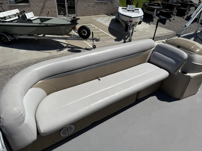 Slide: The Image of 2017 Sweetwater 2286 C pontoon boat with beige seating and nearby trailers. - 19