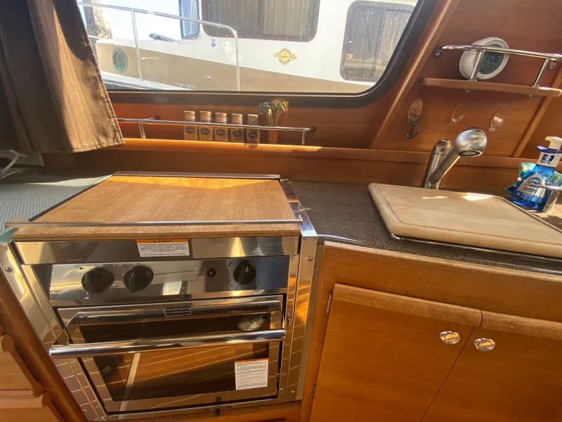 Slide: The Image of 2016 Ranger Tugs R-29S kitchen with stove, sink, and wooden cabinetry. - 22