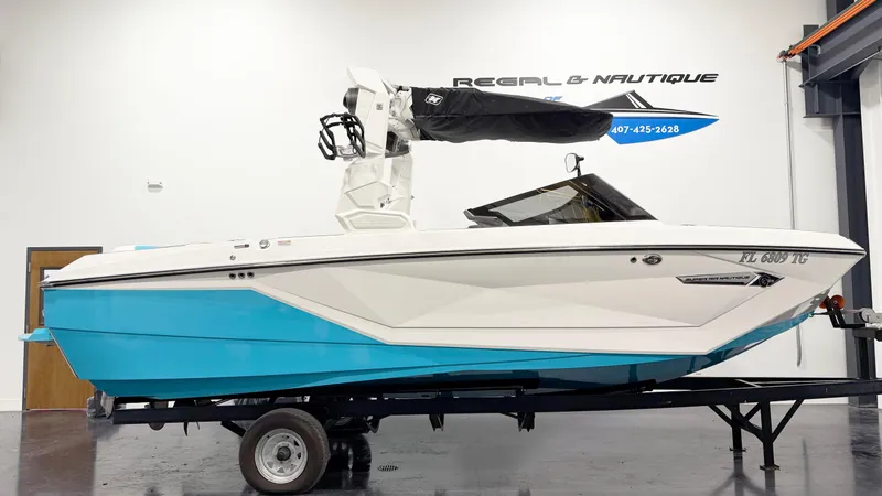 The Image of 2022 Nautique G23 boat in showroom, blue and white design on trailer. - 1