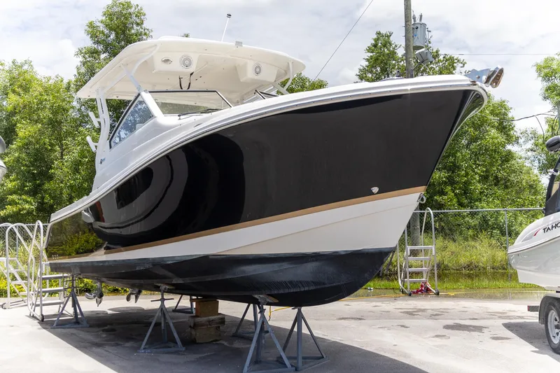 Slide: The Image of 2015 Edgewater 280 CX boat on stands, black and white hull, outdoor setting. - 27
