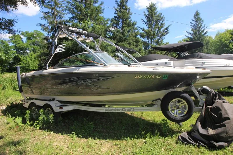 The Image of 2008 MasterCraft X-15 SS boat on trailer, parked outdoors with trees in the background. - 0