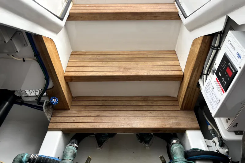 Slide: The Image of Wooden steps in a 2015 Huckins 45 boat engine room, featuring control panel and piping. - 14
