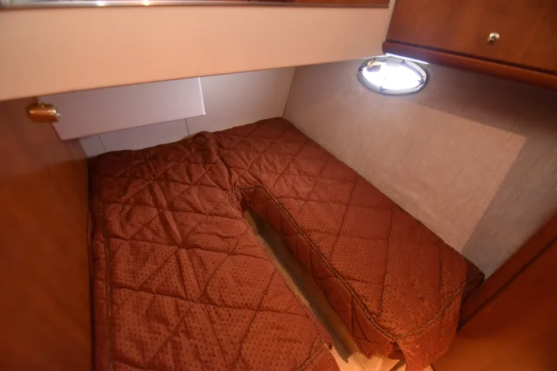 Slide: The Image of 2007 Silverton 38 Convertible cabin with brown quilted bedding and porthole window. - 23