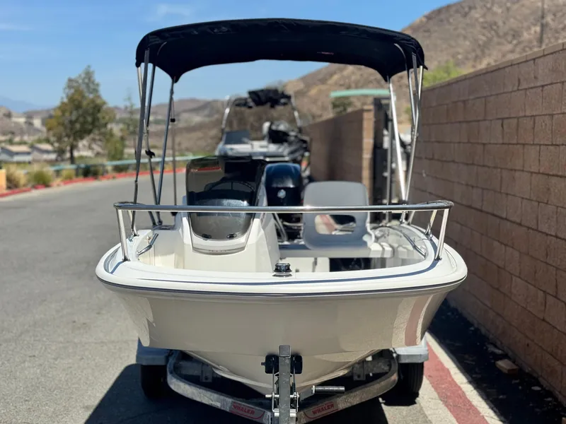 Slide: The Image of 2021 Boston Whaler 130 Super Sport boat on trailer, parked near a brick wall. - 2