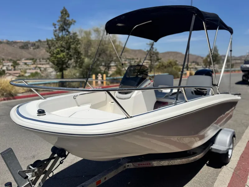 Slide: The Image of 2021 Boston Whaler 130 Super Sport boat on trailer, parked outdoors with scenic background. - 3