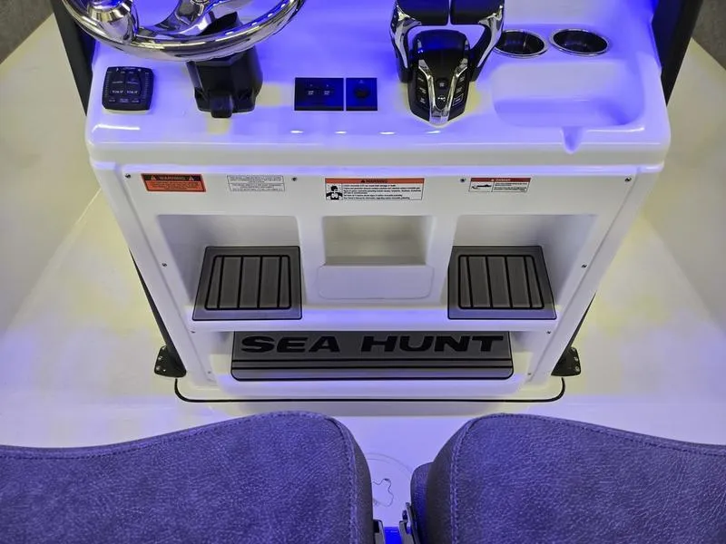 Slide: The Image of 2026 Sea Hunt Ultra 275 SE boat console with controls and seating, illuminated in blue light. - 17