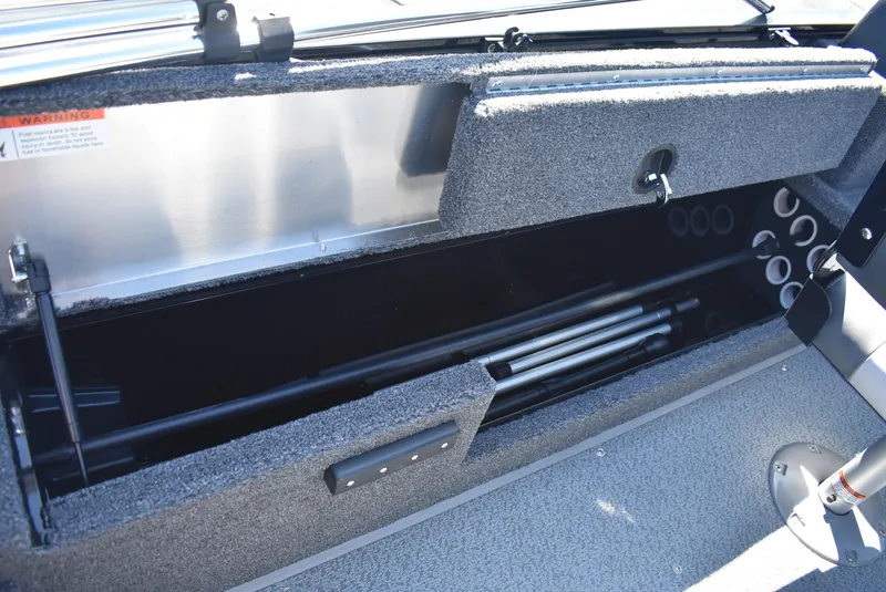 Slide: The Image of 2025 Lowe FM 1675 WT boat storage compartment with rod holders and carpeted interior. - 17
