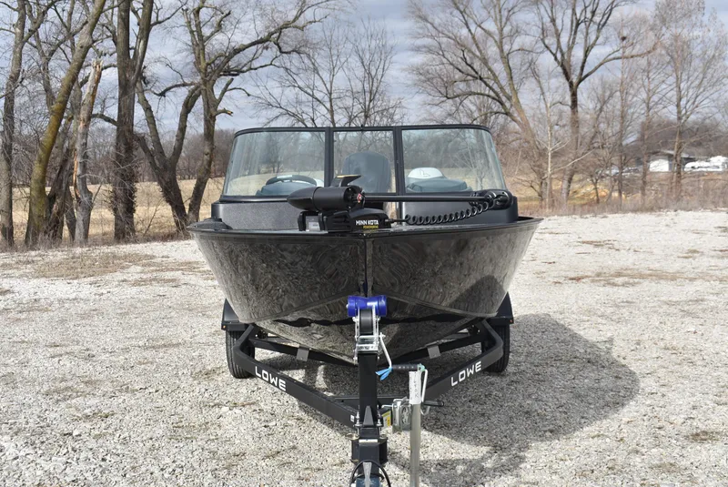 Slide: The Image of 2025 Lowe FM 1675 WT boat on trailer, parked outdoors with trees in background. - 2