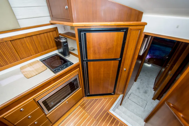 Slide: The Image of 1999 Riviera 43 Open Flybridge kitchen with wood cabinetry, stove, microwave, and refrigerator. - 26