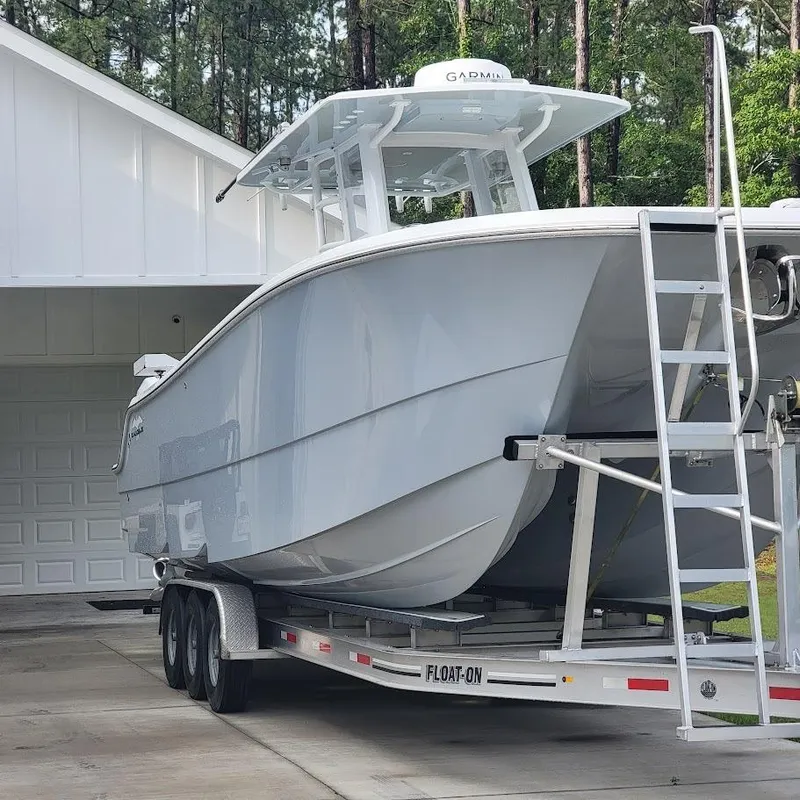 Slide: The Image of 2022 Invincible 33 Catamaran on trailer, parked near a garage, surrounded by trees. - 3