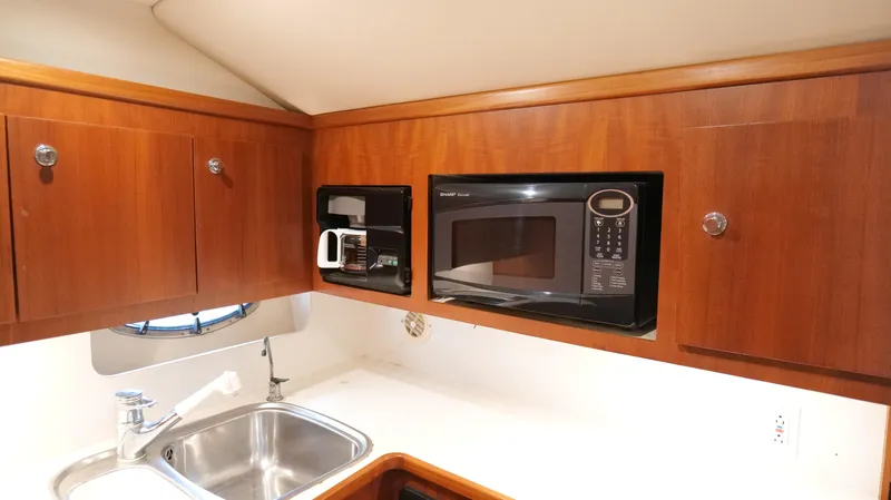 Slide: The Image of 2000 Tiara Yachts 3700 Open kitchen with microwave, sink, and wooden cabinets. - 37