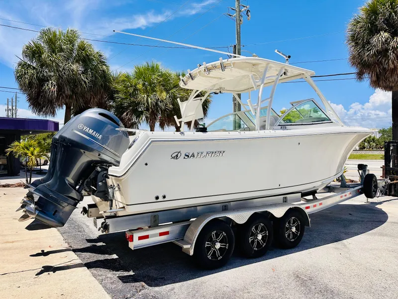 Slide: The Image of 2014 Sailfish 275 DC boat on trailer with Yamaha engine, parked near palm trees. - 2