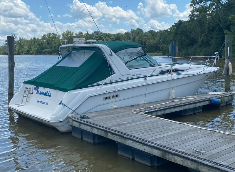 The Image of 1993 Sea Ray 370 Sundancer docked by a scenic river under a cloudy sky. - 0