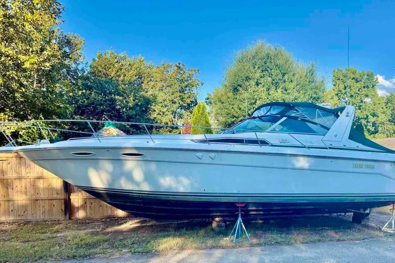 Slide: The Image of 1993 Sea Ray 370 Sundancer boat on land, surrounded by trees and a wooden fence. - 2
