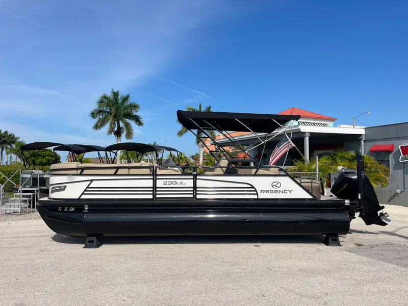 Slide: The Image of 2019 Regency 230 LE3 pontoon boat with canopy, parked outdoors under clear blue sky. - 8