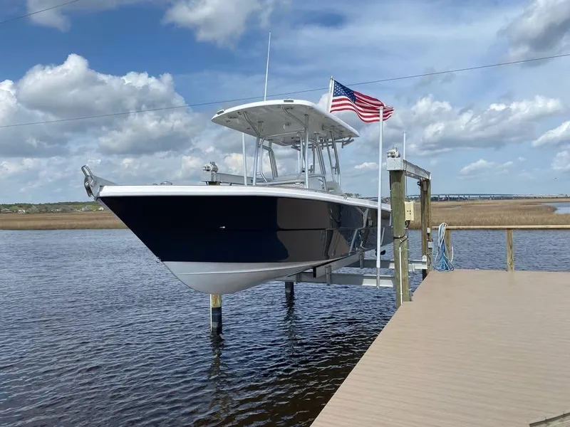 Slide: The Image of A 2025 Custom Shark Fin R321 boat docked, with an American flag, under a partly cloudy sky. - 6