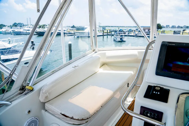 Slide: The Image of 2002 Cabo 47 Flybridge Sportfisher interior with marina view, featuring cushioned seating and navigation equipment. - 13