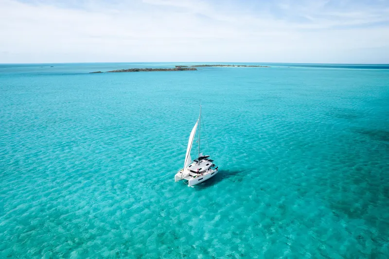 Slide: The Image of 2023 Lagoon 40 catamaran sailing in clear turquoise waters, distant island view. - 3