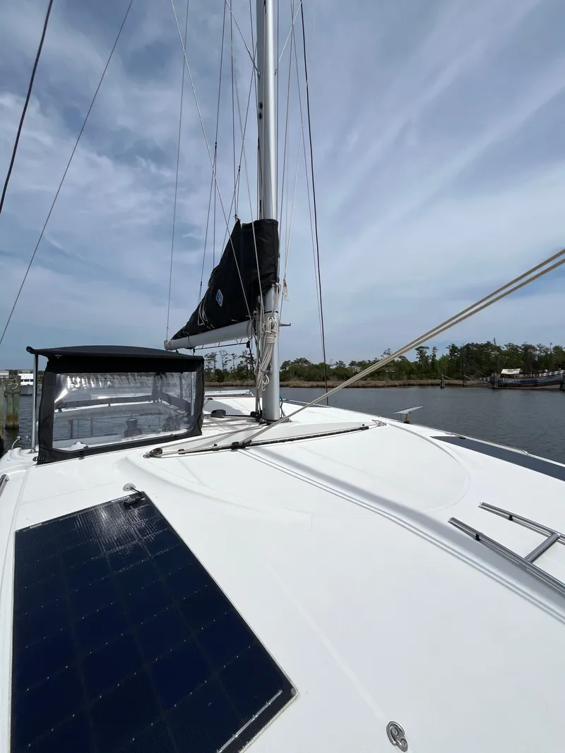 Slide: The Image of 2023 Lagoon 40 sailboat deck with solar panel and mast, docked by a calm waterway. - 48
