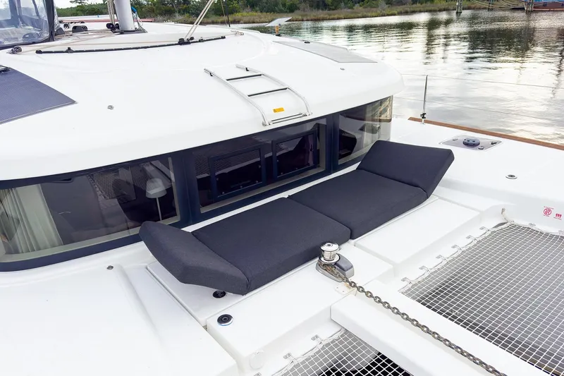 Slide: The Image of 2023 Lagoon 40 catamaran with cushioned deck seating, docked by calm waters. - 50