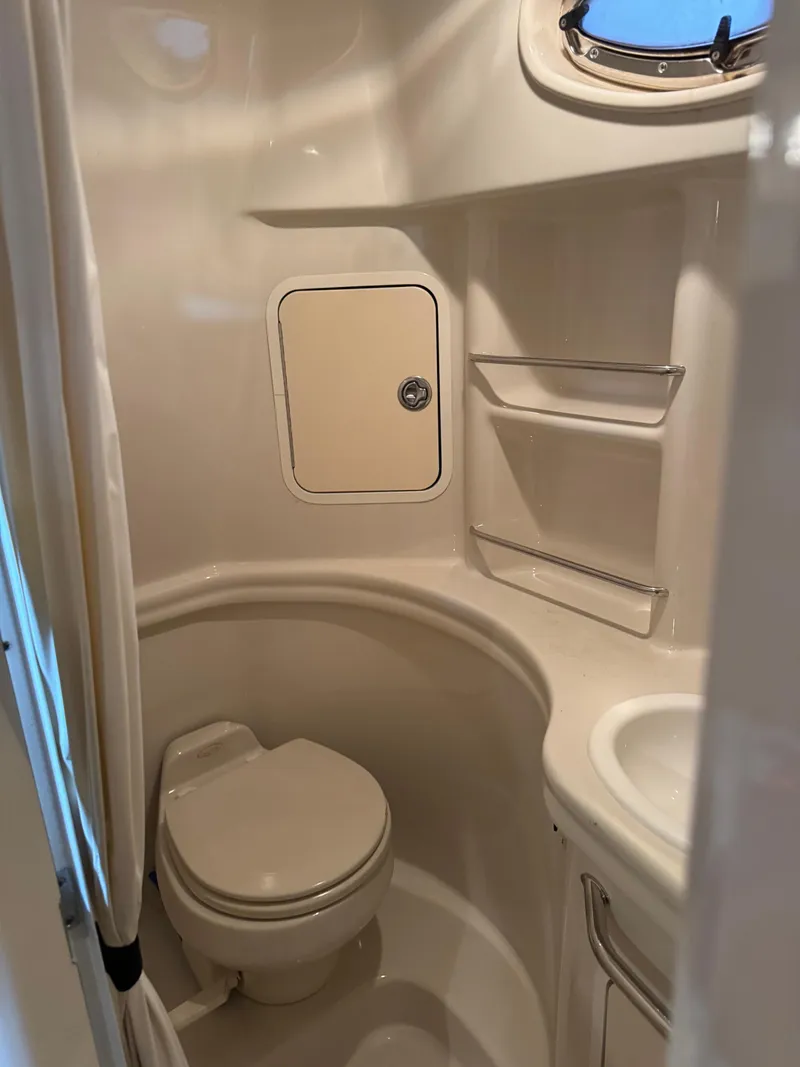 Slide: The Image of Compact bathroom in 2005 Sea Ray 300 Sundancer boat, featuring toilet, sink, and storage shelves. - 16