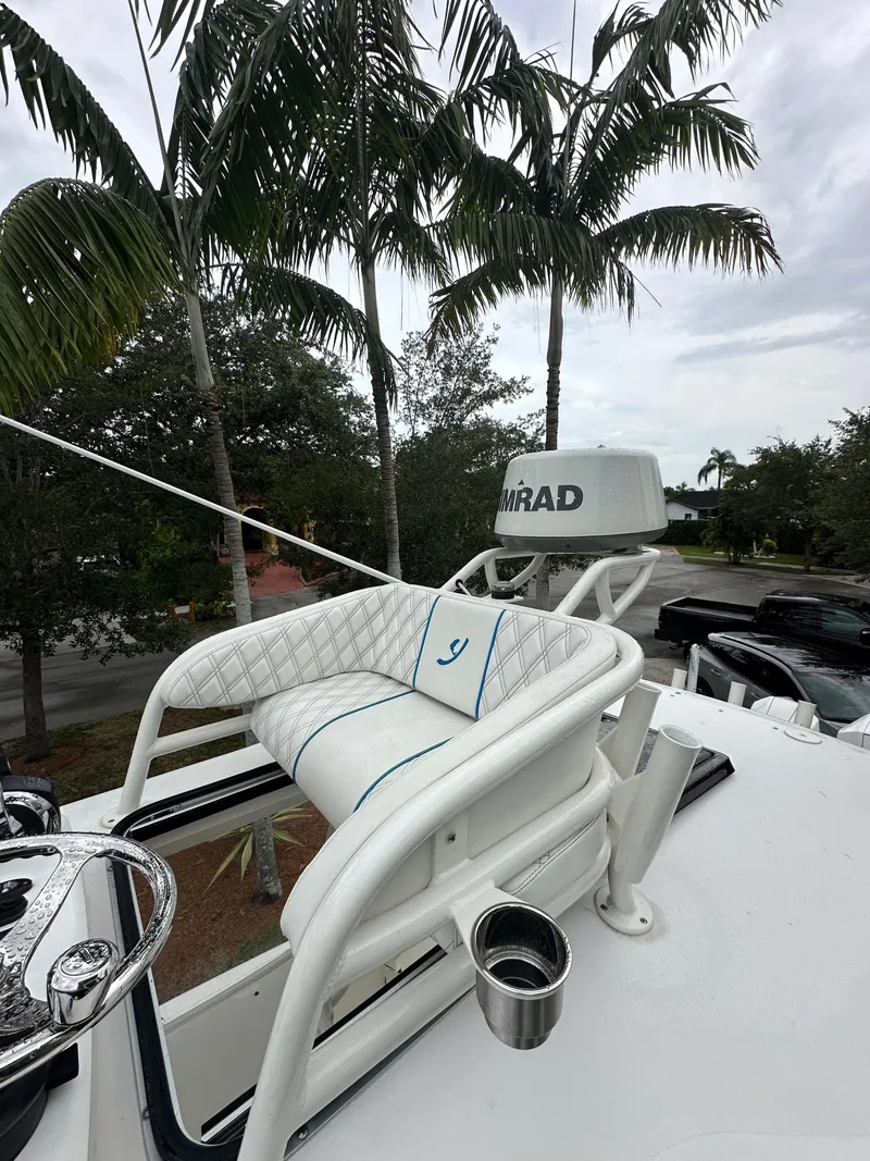 Slide: The Image of White boat helm with cushioned seat, palm trees in background, overcast sky. - 14