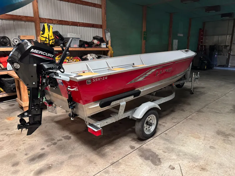 The Image of 2023 Lund SSV-14 Tiller boat on trailer in garage with Mercury outboard motor. - 0