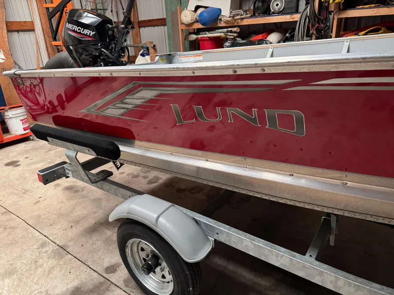 Slide: The Image of 2023 Lund SSV-14 Tiller boat on trailer in garage with Mercury outboard motor. - 4