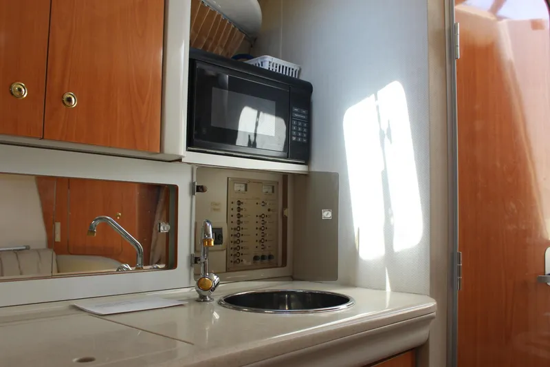 Slide: The Image of 2000 Regal Commodore 2760 boat interior with kitchenette, featuring sink, microwave, and wooden cabinets. - 19