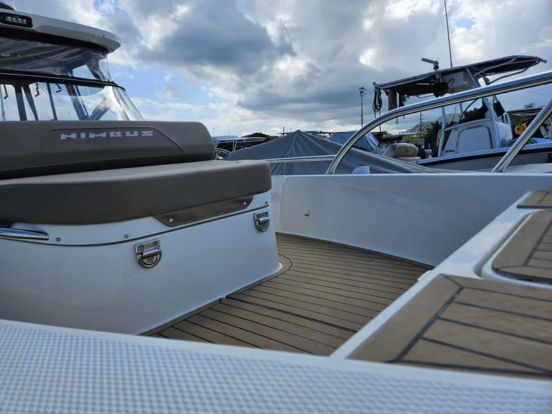 Slide: The Image of 2023 Nimbus Tender 8 boat interior with cushioned seating and wooden deck under cloudy sky. - 9